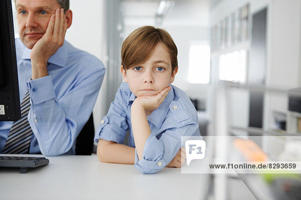 Boy leaning on elbow  father using computer