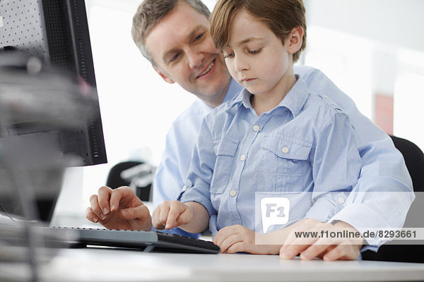 Junge sitzt auf Vaters Schoß mit Computertastatur