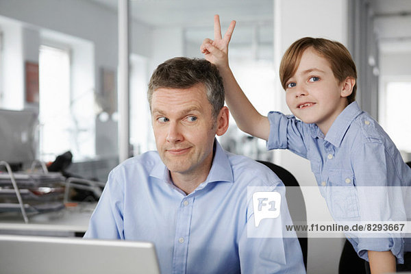 Vater mit Laptop,  Sohn macht Friedenszeichen hinter dem Kopf