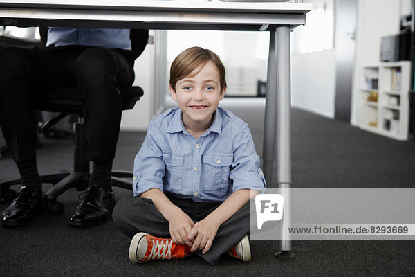 Boy sitting on floor with businessman working at desk