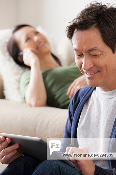 Reifer Mann mit digitalem Tablett  Frau auf dem Sofa liegend
