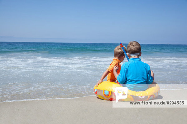 Zwei junge Brüder sitzen auf einem Gummiring am Strand.