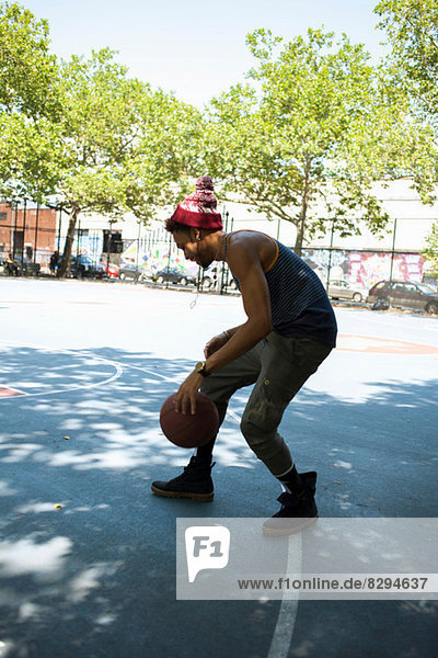 Junger Mann dribbelt Basketball auf dem Freigelände
