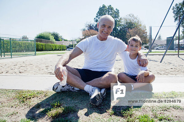 Großvater und Enkel sitzend auf dem Sportplatz
