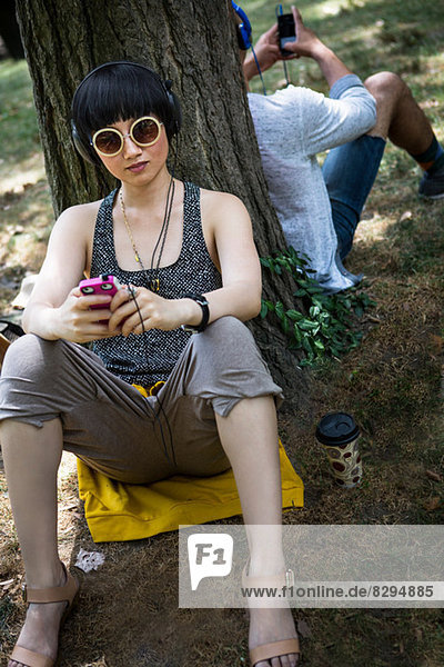 Young woman leaning against tree trunk with mp3 player