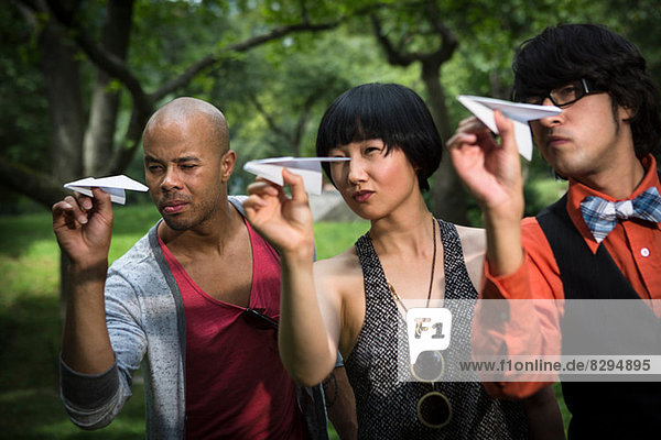 Three friends throwing paper planes in park