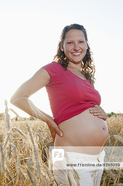 young pregnant woman standing in cornfield
