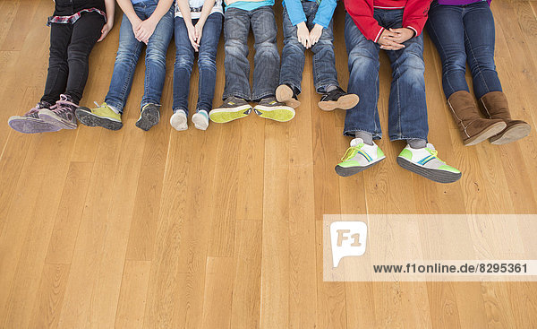 Österreich  Kinder und Jugendliche sitzen auf einem Holzboden und zeigen ihre Beine.