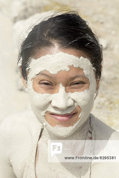Italien  Sizilien  Porträt einer lächelnden Asiatin mit Schlammmaske