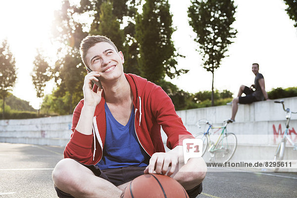 Junger Mann mit Smartphone und Basketball
