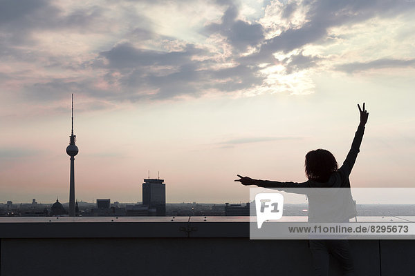 Young woman on rooftop terrace  raising arms
