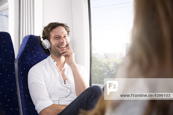 Mann mit Kopfhörern im Zug lächelt Frau an
