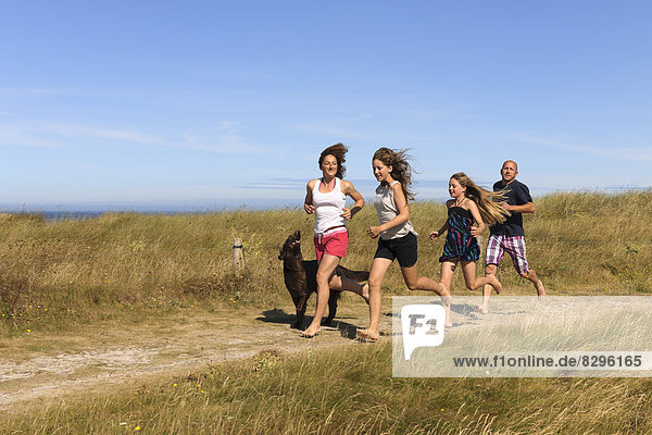 France  Bretagne  Ste Marguerite  Landeda  Finistre  parents and two daughters running with her dog on a dune at Atlantic