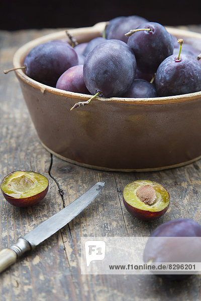 Earthenware bowl with plums and a knife on wooden table  studio shot