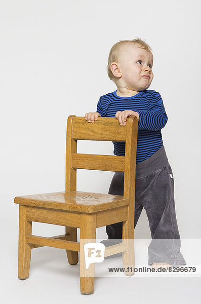Kleiner Junge mit traurigem Gesicht  der sich am Stuhl festhält  Studioaufnahme