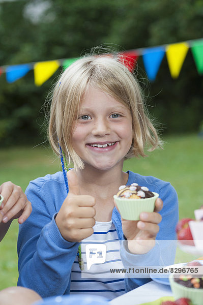 Glückliches Mädchen beim Muffinessen auf einer Geburtstagsparty