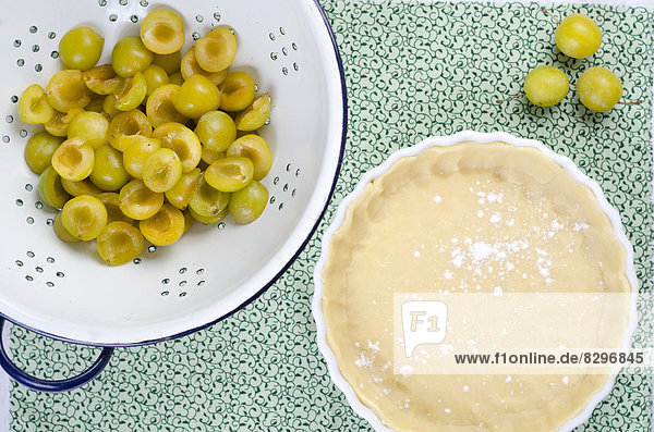 Raw short pastry in baking dish and colander with mirabelles on a table