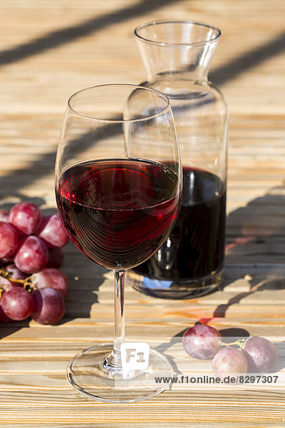 Glas und Karaffe mit Rotwein und roten Trauben am Holztisch