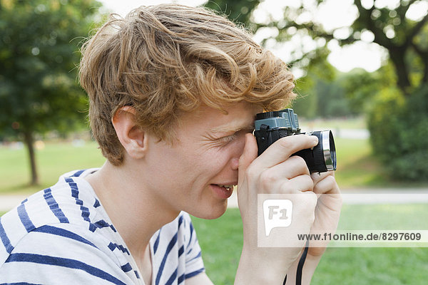 Young man taking a picture in park with an old-fashioned camera