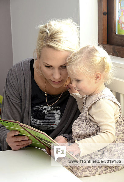Mutter schaut mit ihrer kleinen Tochter ein Buch an
