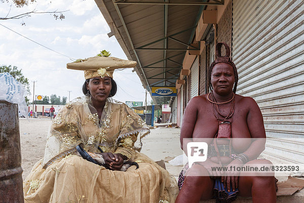Herero-Frau und Himba-Frau in traditioneller Kleidung sitzen nebeneinander