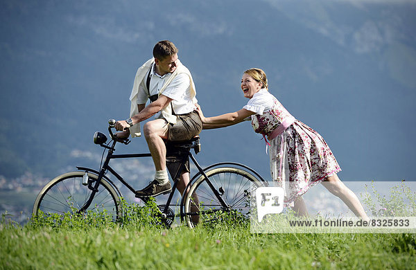Man and a woman wearing traditional costume with an old bicycle within a natural landscape