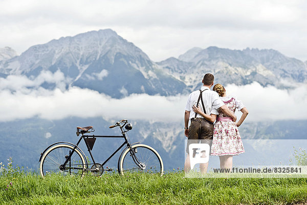 Mann und Frau in Tracht mit einem alten Fahrrad blicken auf die Berge