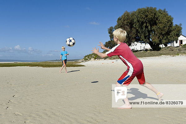 Jungen spielen Fußball am Strand