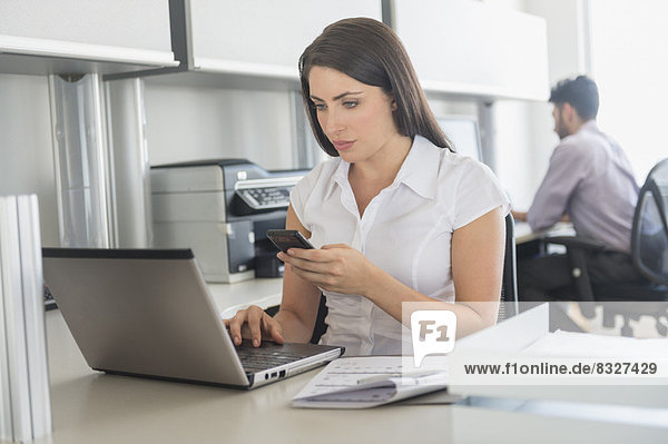 Woman working on laptop and text messaging in office  man in background