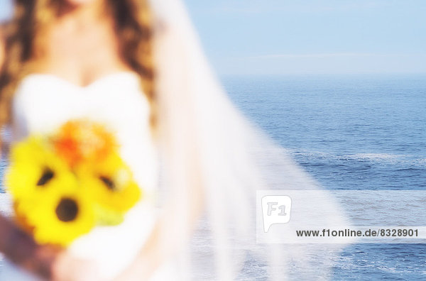 Mid section of bride holding sunflower bouquet  sea in background
