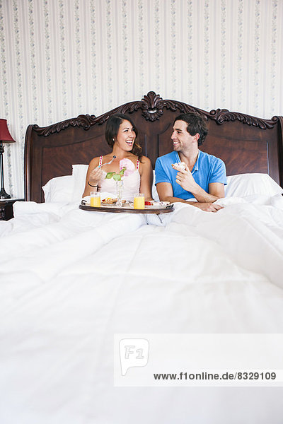Young couple eating breakfast in bed in hotel room