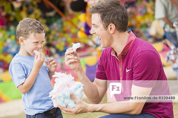 Happy father with son (4-5) in amusement park eating cotton candy