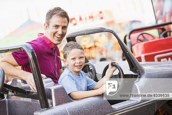 Father with son (4-5) driving toy car in amusement park