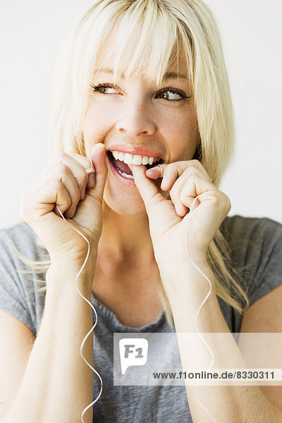 Studio portrait of blonde woman cleaning teeth with dental floss