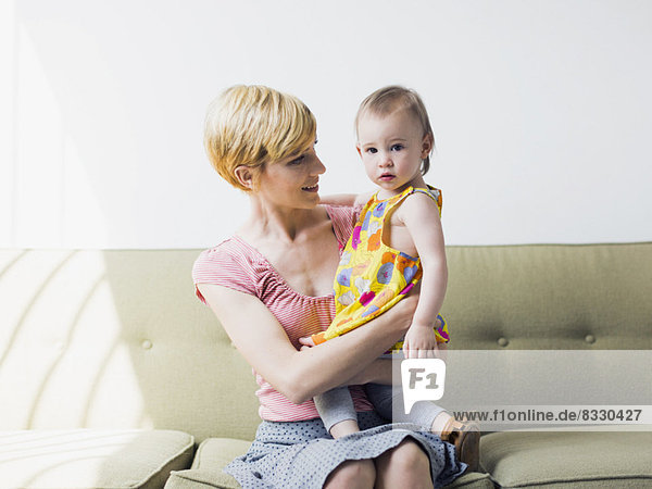 Mother with daughter (12-17 months) sitting on sofa