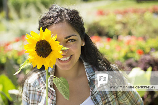 Ein Bauernhof  der biologisches Gemüse und Obst anbaut und verkauft. Eine Frau  die eine große Sonnenblume hält.