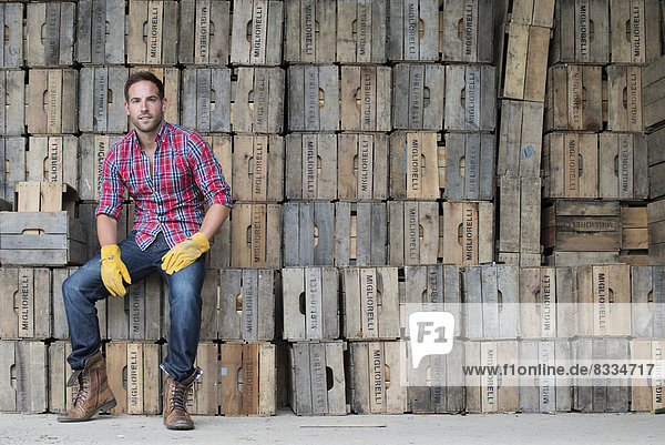 A farmyard. A stack of traditional wooden crates for packing fruit and vegetables. A man sitting on a packing case.