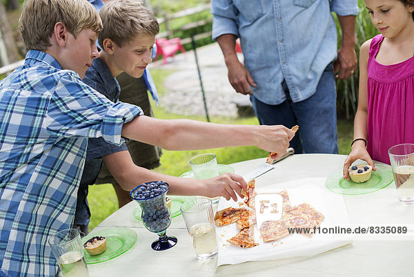 Biologische Landwirtschaft. Eine Familienfeier im Freien mit Picknick. Erwachsene und Kinder. Ein Teller Pizza.