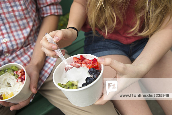 Junge Leute sitzen Seite an Seite und essen frisches Bio-Obst und Joghurt-Dessert.