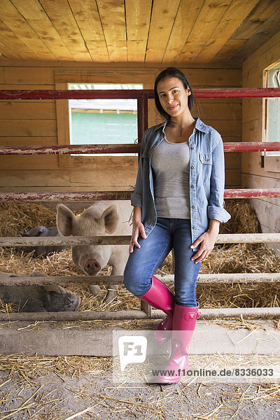 Ein Bio-Bauernhof in den Catskills. Eine Frau neben einem Schwein im Stall  im tiefen Stroh stehend.