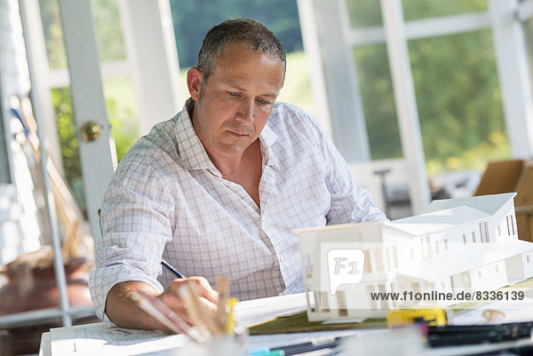 A farmhouse kitchen. A model of a house on the table. Designing a house. A man using a pencil drawing on a plan.