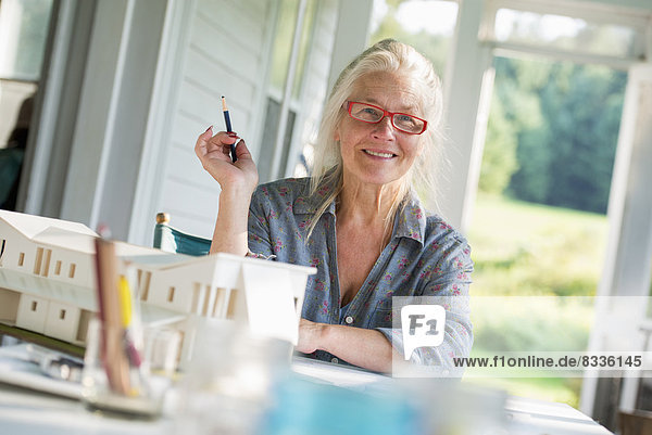 Eine Bauernhaus-Küche. Ein Modell eines Hauses auf dem Tisch. Ein Haus entwerfen. Eine Frau sitzt und hält einen Stift.