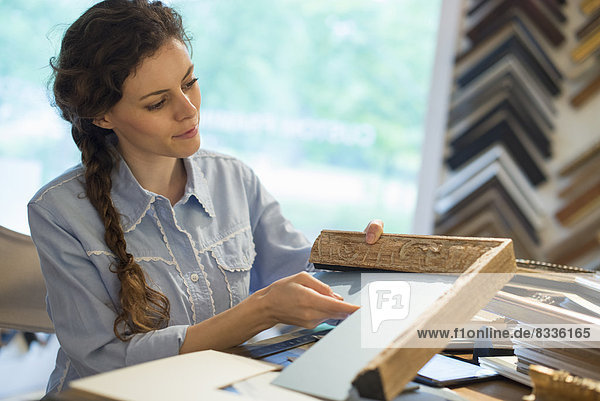 Eine Frau in der Werkstatt eines Bilderrahmers bei der Auswahl von Rahmen und Passepartouts. Umgeben von Mustern.