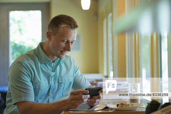 A man with short cropped hair sitting at a cafe table  using a smart phone.