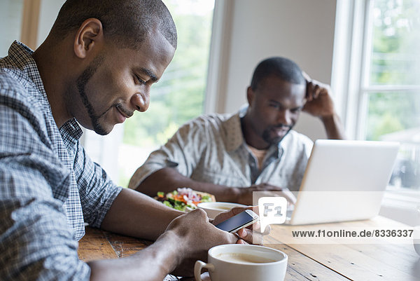 Zwei Männer sitzen in einem Cafe. Mit einem Laptop und einem Smartphone.