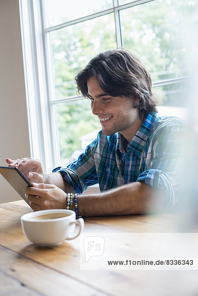 Ein Mann sitzt in einem Café mit einer Tasse Kaffee. Mit einem digitalen Tablet.
