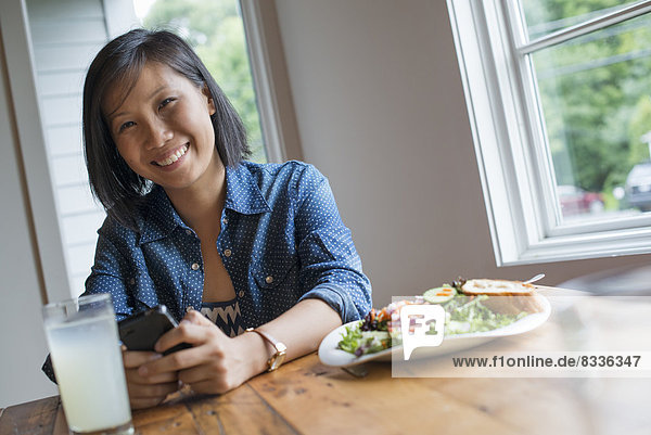 Eine junge Frau mit einem Smartphone  an einem Tisch sitzend. Kaffee und ein Sandwich.
