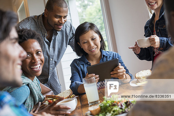 Eine Gruppe von Menschen  die sich in einem Café zu einer Mahlzeit trifft. Mit digitalen Tablets und Smartphones.