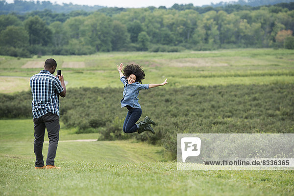 Ein Mann fotografiert eine Frau  die in die Luft springt und vor Freude mit ausgestreckten Armen springt.