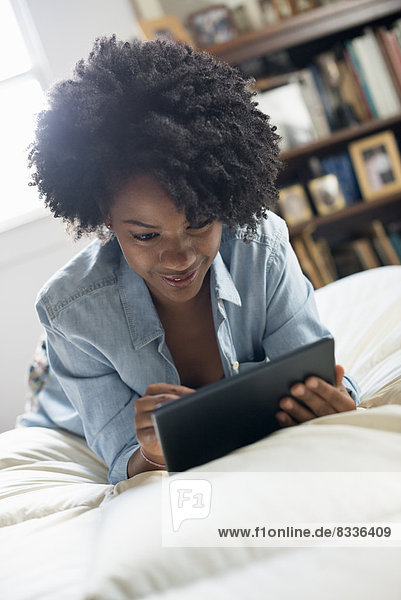 A woman lying on a bed  using a digital tablet.